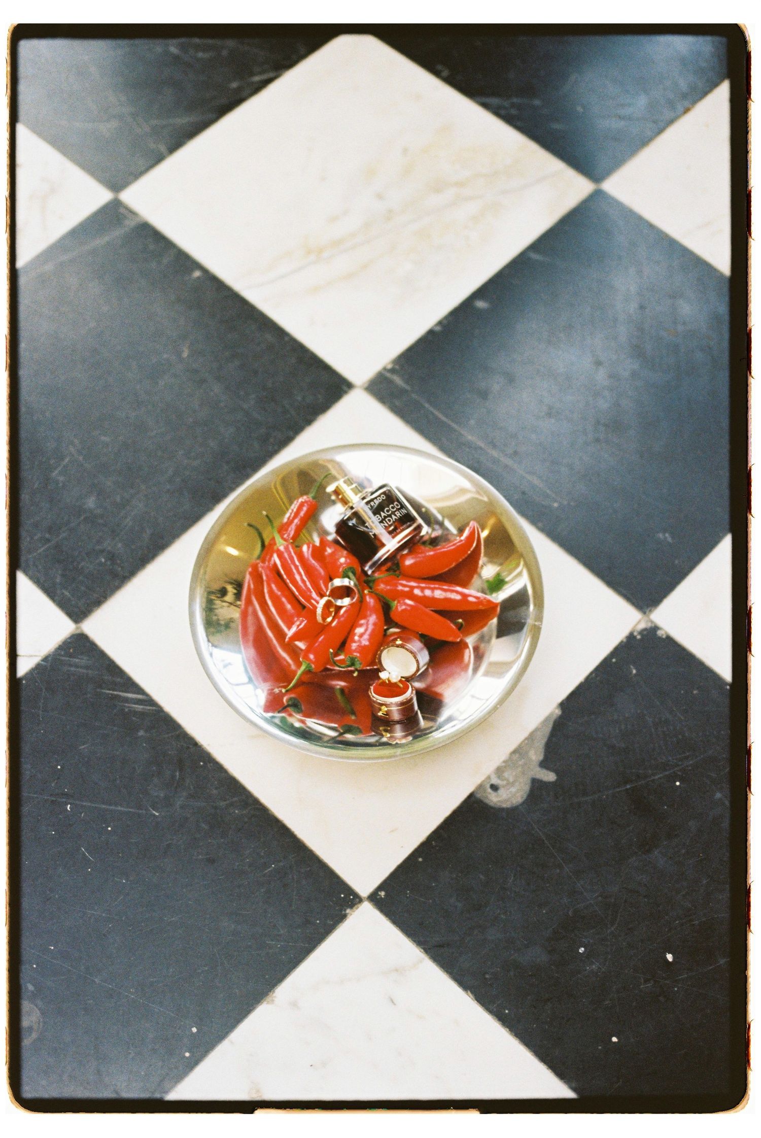 Red chili peppers and a lighter arranged on a silver dish atop a classic black and white checkered floor.