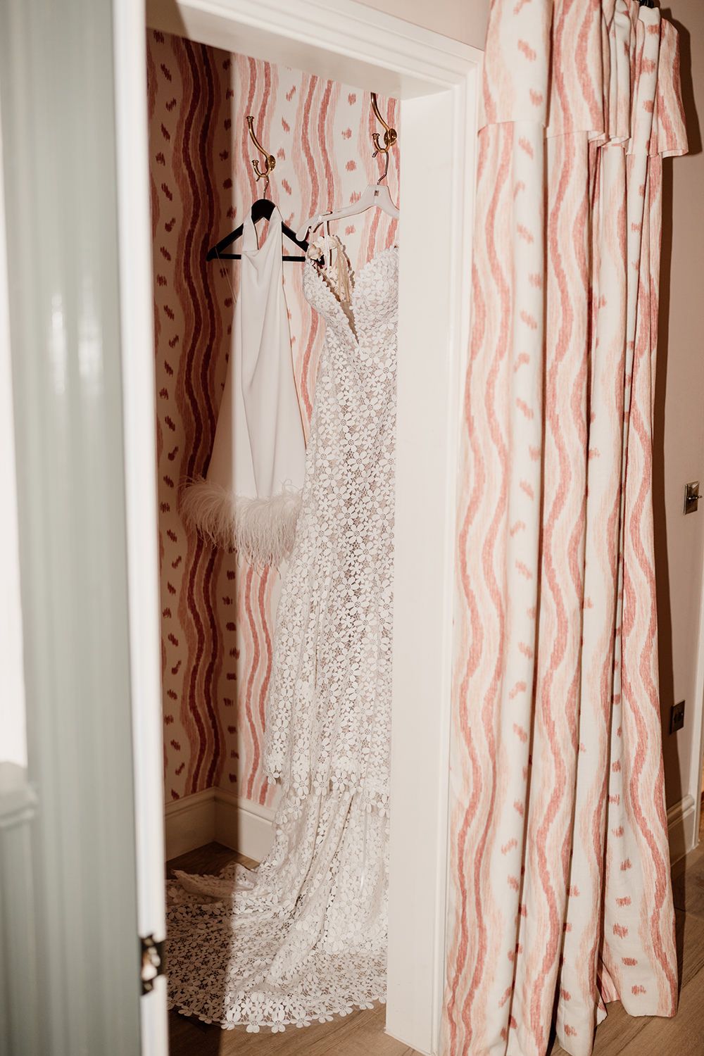 White wedding dress and pink curtains hanging in a brightly lit dressing room before the ceremony.