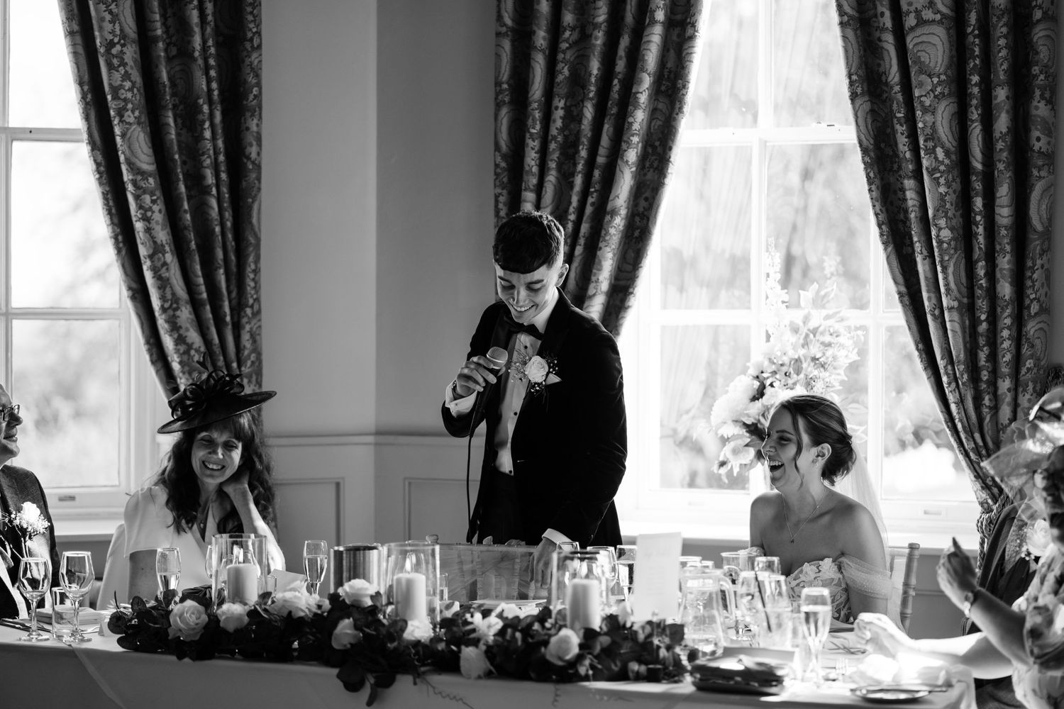 Groom making a speech on his wedding day with windows behind him.