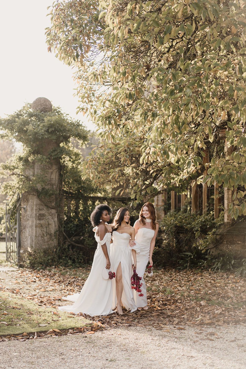 Three people in white dresses sharing special moments together on a garden path surrounded by trees during a photoshoot.