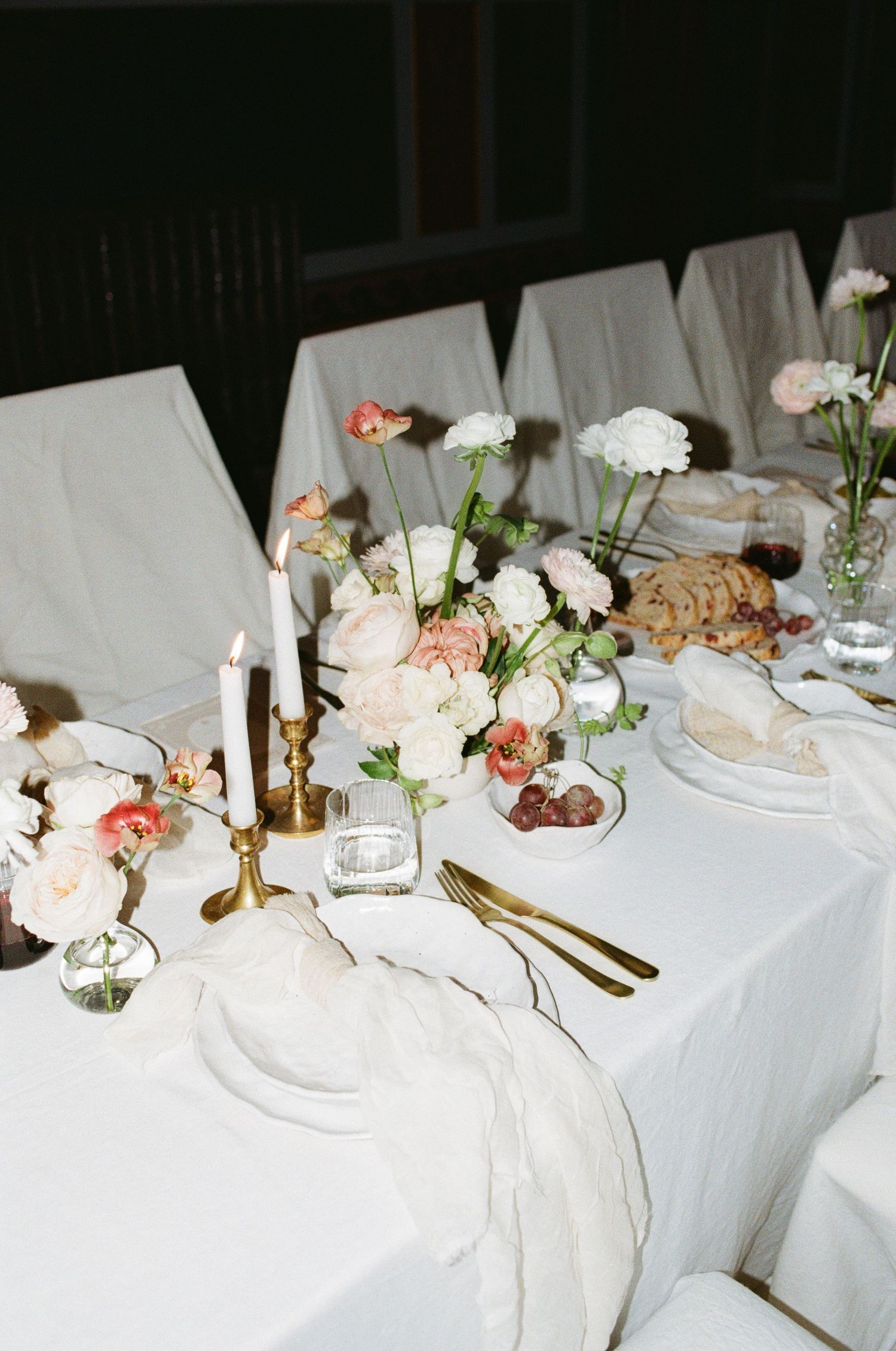 An elegant table setting with white linens, brass candlesticks, pink and white flowers in delicate vases, and golden cutlery.