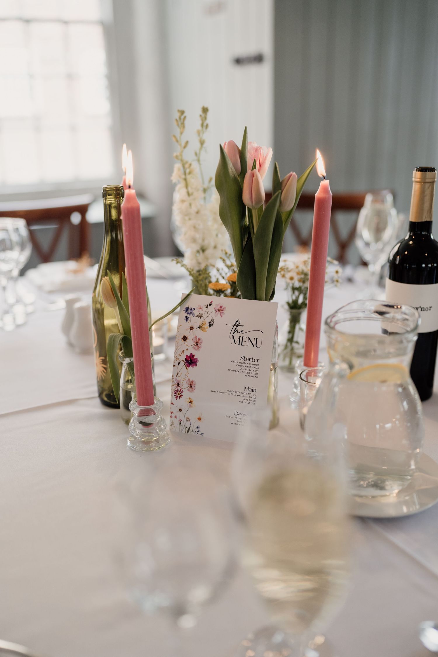 Elegant table setting with pink tulips, lit candles, and wine bottles for a formal dinner.