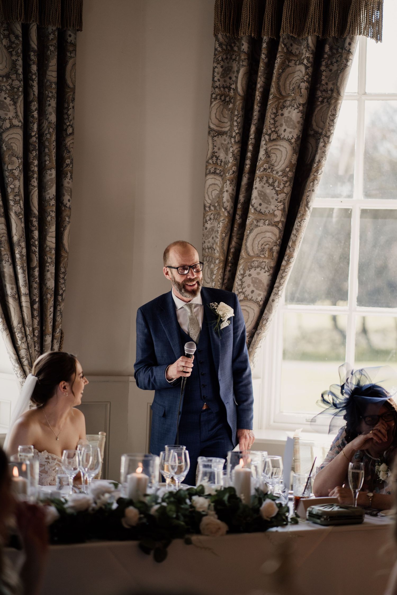 Father of the bride doing a wedding day speech while the bride looks towards him.