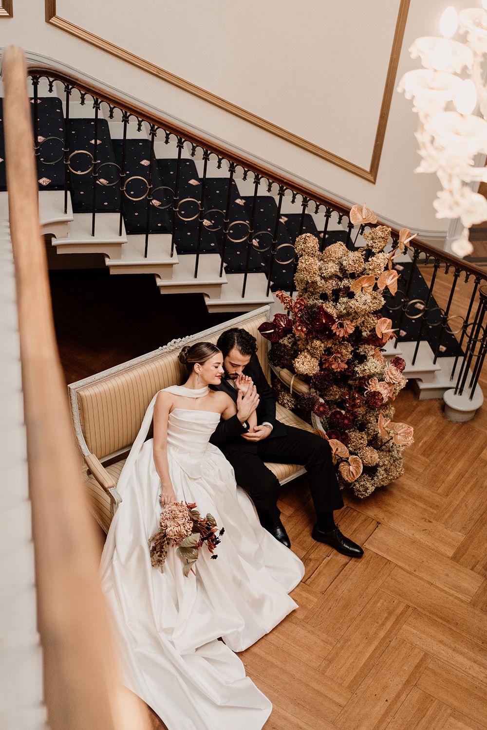Bride and groom snuggled on a sofa surrounded by autumnal flowers at Rise Hall.