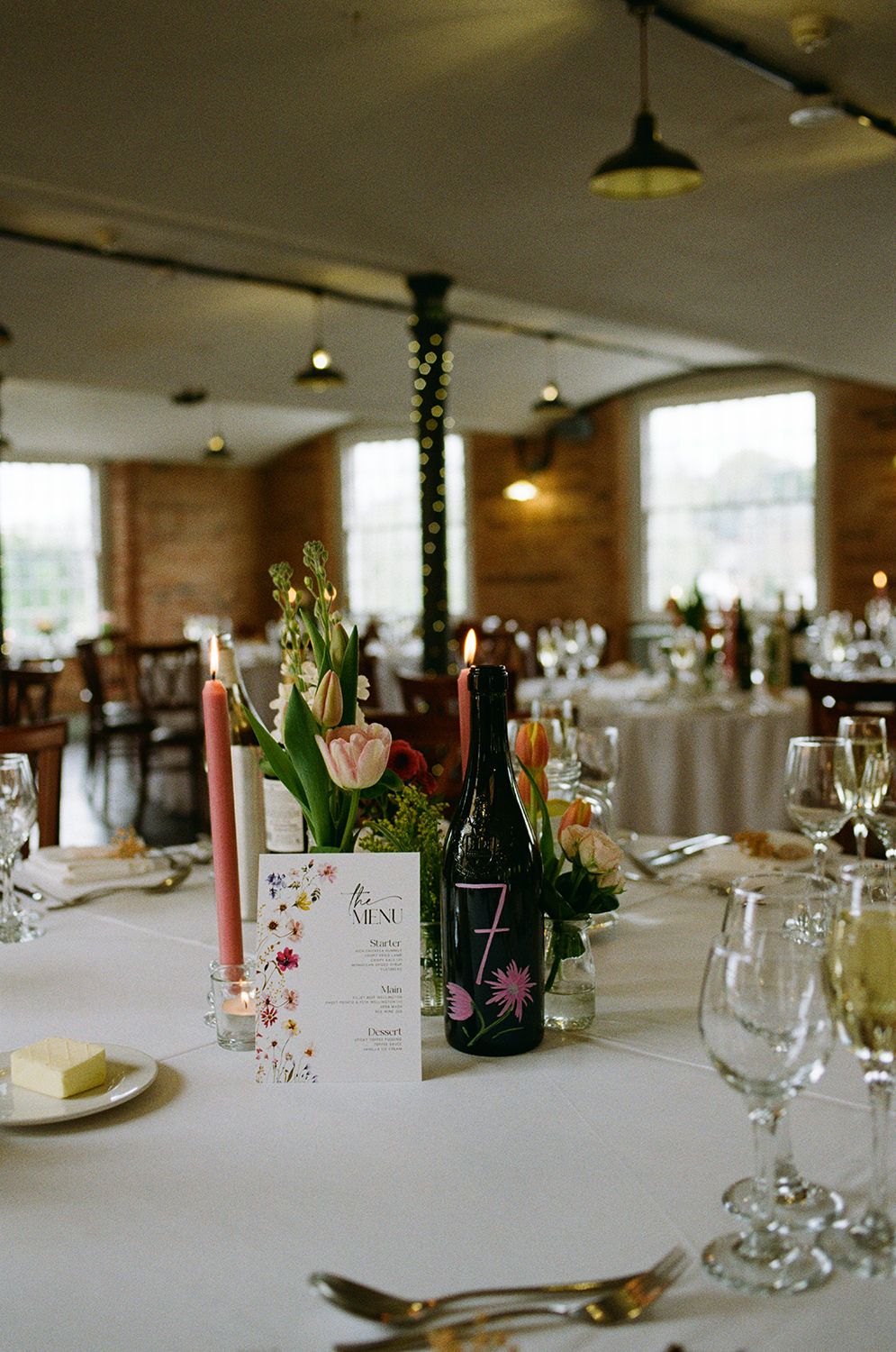 Wedding reception room at The West Mill styled with pastel wild flowers and personalised menu stationery.