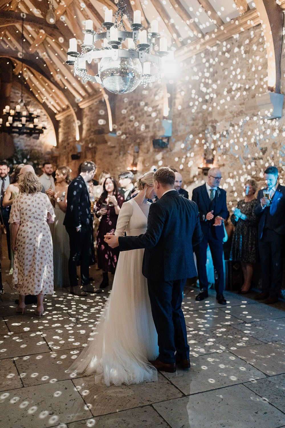 Bride and groom dancing under the disco ball at Healey Barn with guests watching stood in a circle.