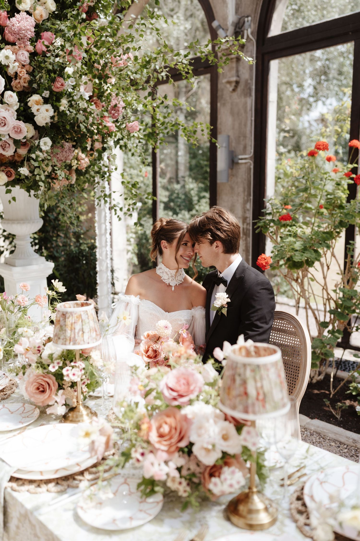 Bride and groom sharing an intimate moment at a floral-adorned reception table in a greenhouse.