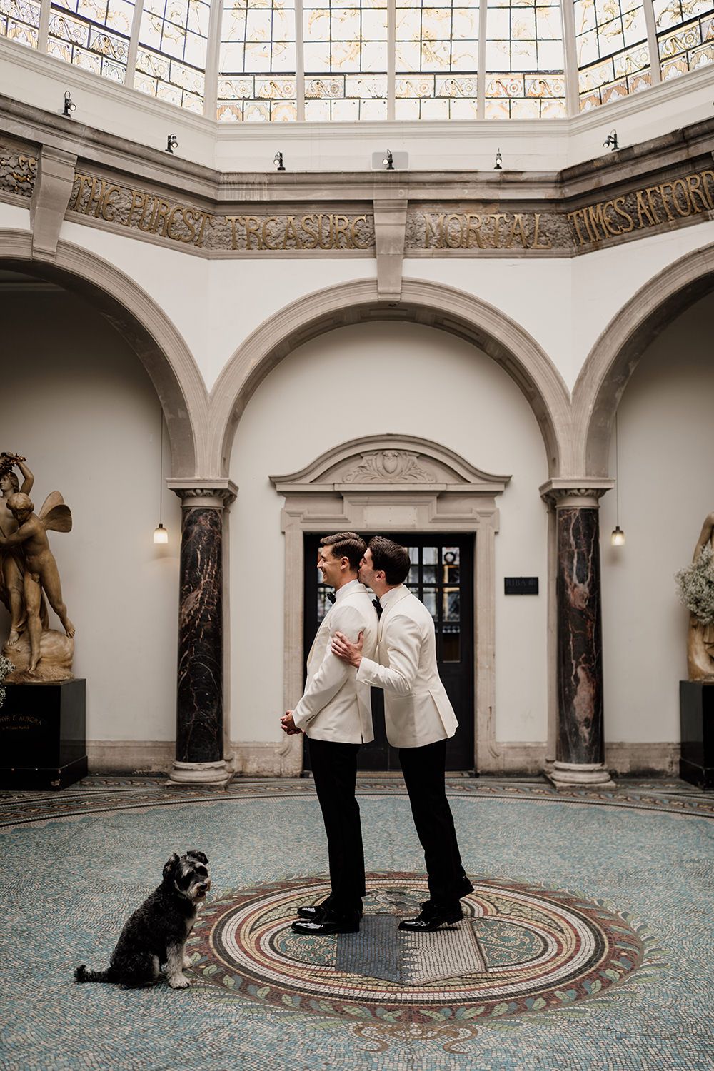 Two grooms doing a first look at Battersea Arts Centre, one is kissing the other from behind wearing matching outfits.