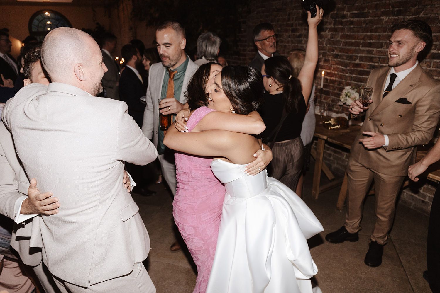 Wedding guests dancing and celebrating on the dance floor at a reception in a rustic brick-walled venue.