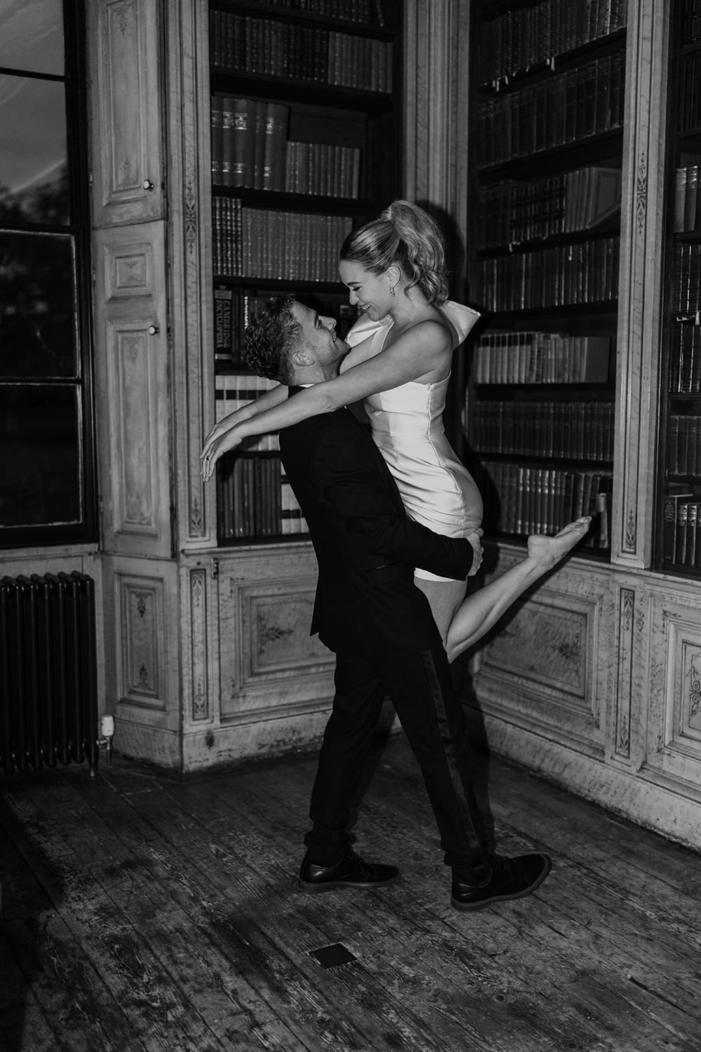 Bride and groom dancing and laughing with each other at night time in the library in Rise Hall.