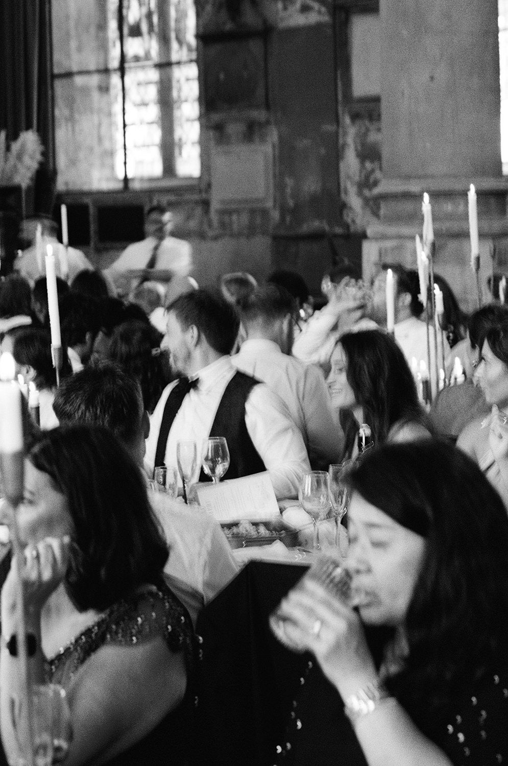 Black and white photo of wedding reception guests dining at tables with tall white candles.