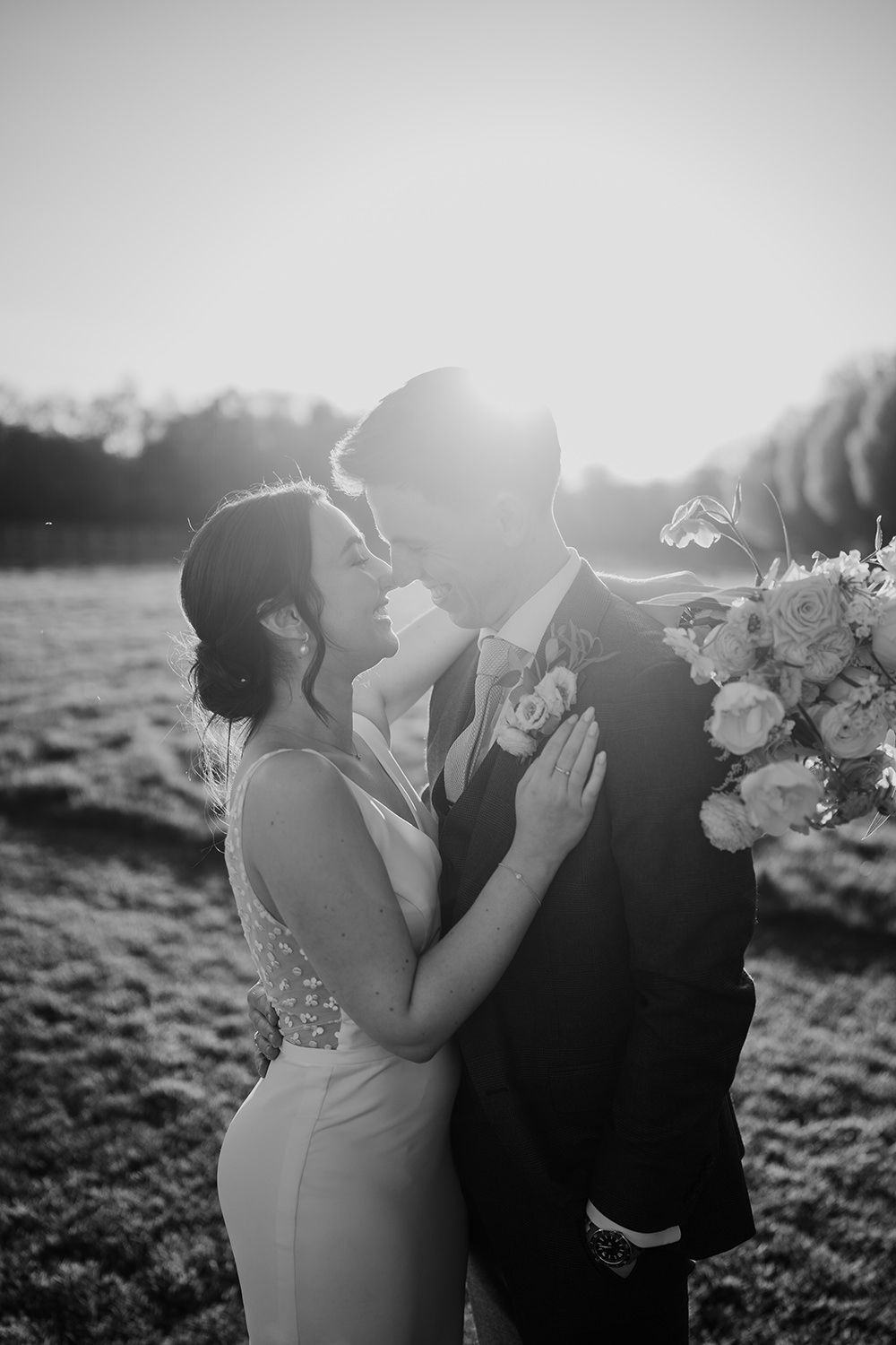 Bride and groom stood looking towards each other with the sun setting, the bride is holding her wedding bouquet.
