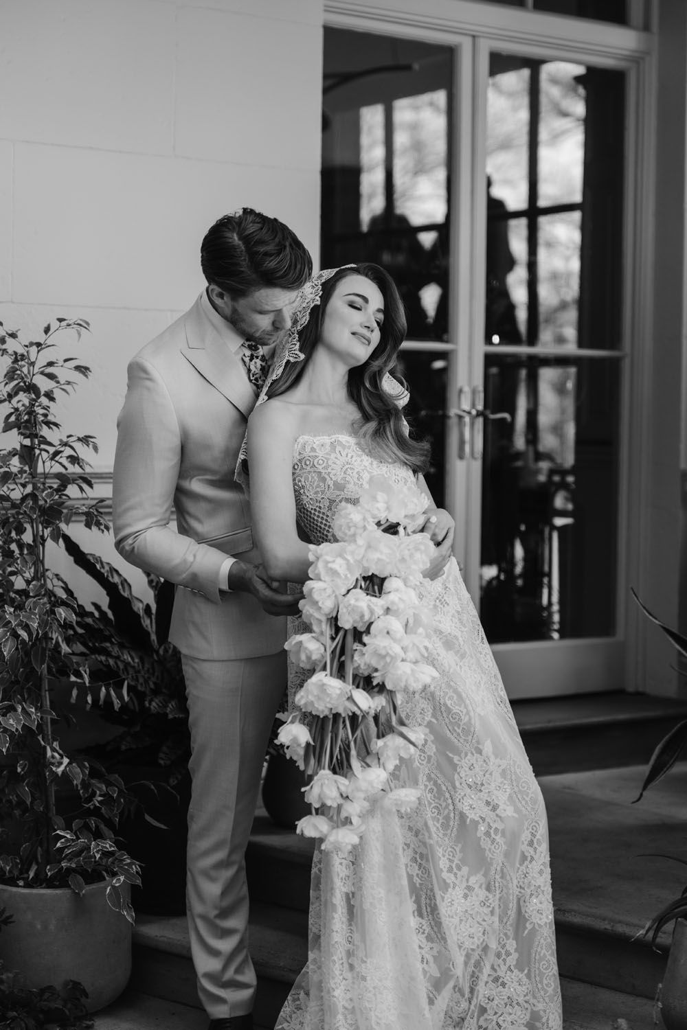 Black and white wedding photo of bride in lace gown holding cascading rose bouquet with groom in suit on elegant steps.