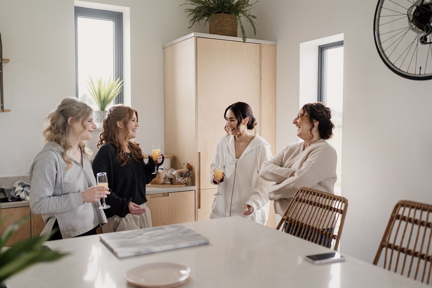 Bride and bridesmaids stood talking by a kitchen island in a bright white kitchen.