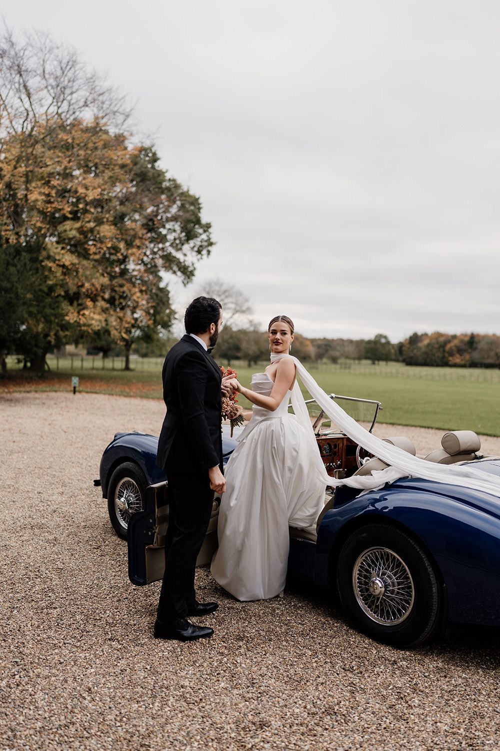Bride and groom in the grounds at Rise Hall while the bride steps out of a vintage car.