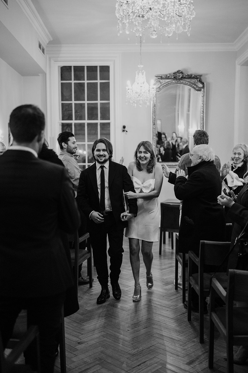 A sequence of black and white photos showing an elegant indoor party scene with people mingling under crystal chandeliers.