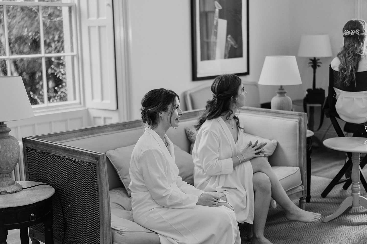 Bridesmaids sat on sofa waiting for hair and makeup on wedding morning.