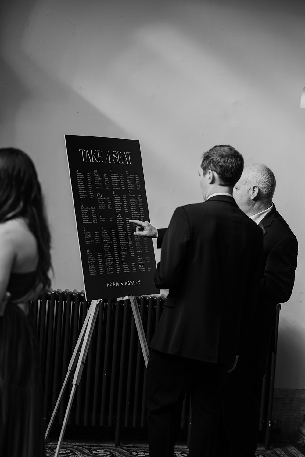 Two wedding guests reading the order of the day at a wedding, they're wearing suits.