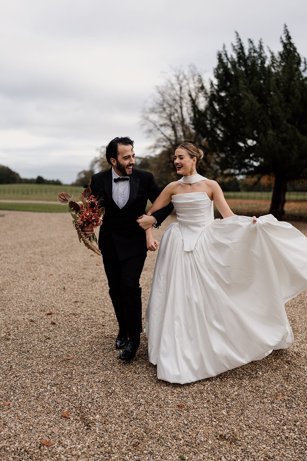 Bride and groom running in the grounds of Rise Hall, holding autumnal flowers while laughing and smiling.