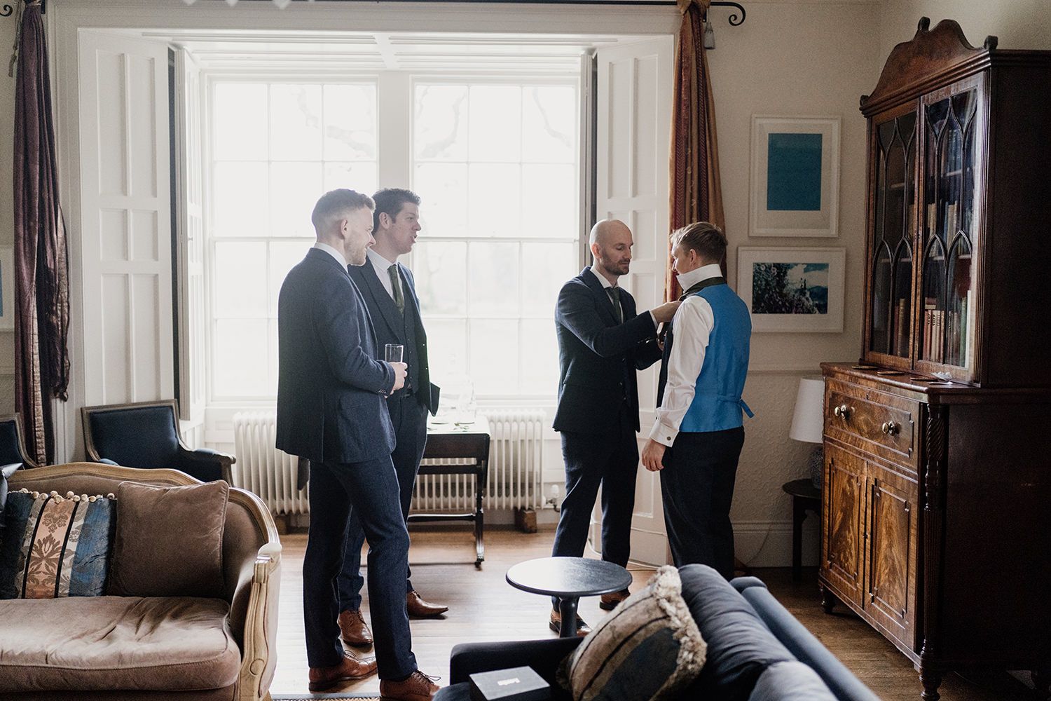 Groomsmen helping groom put on tie in a grand dining room at Healey Hall.