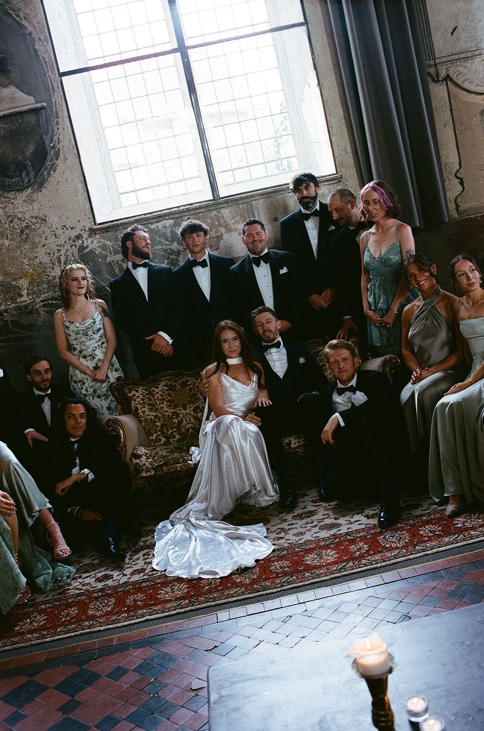 A wedding party sits on the floor in an industrial space with exposed brick walls and a decorative rug.