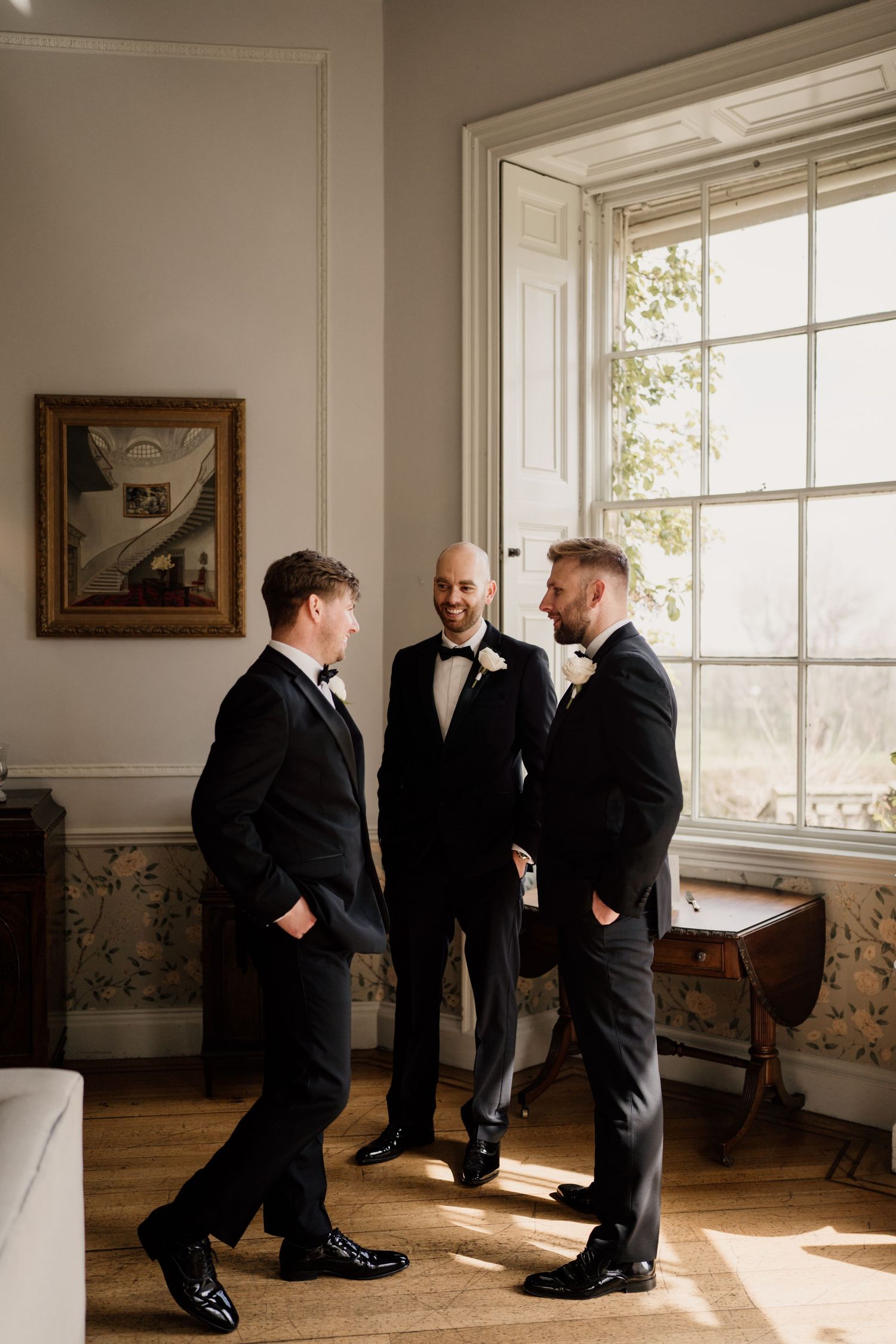 Groomsmen talking in window light at middleton lodge estate.