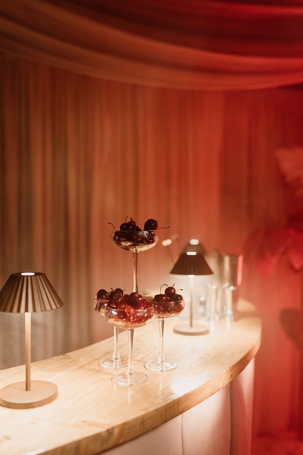 A row of distinctive lamps with curved shades illuminates a white surface in a red-tinted room creating moody ambiance.