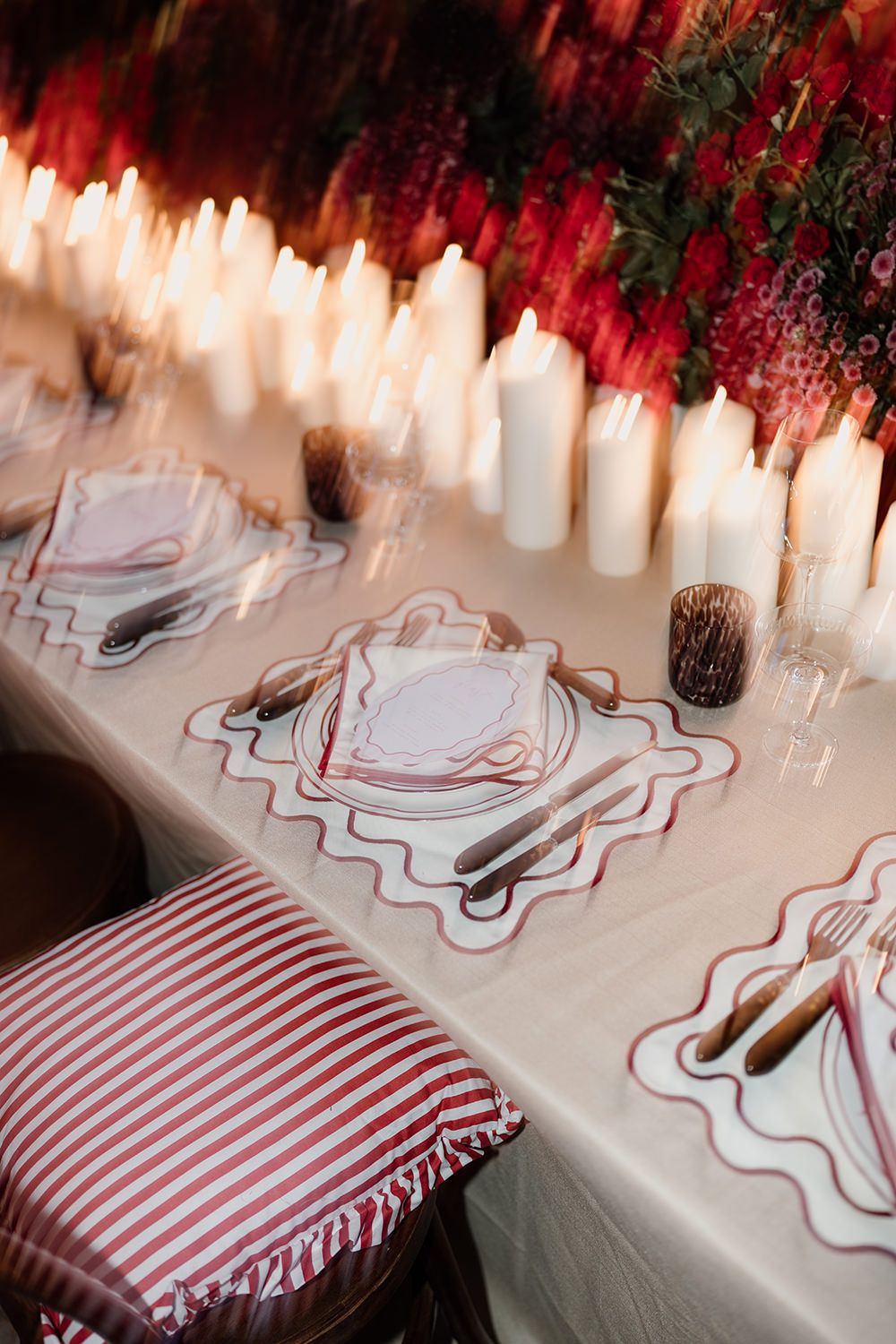 Elegant table setting with white candles and red striped cushions featuring wavy placemats and festive Christmas decorations.