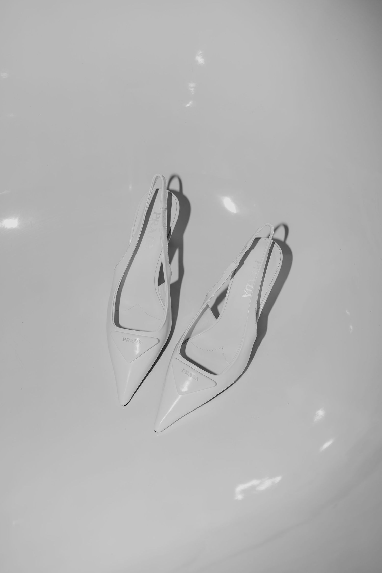 Black and white minimalist photograph of elegant white pointed-toe slingback heels against a light background.