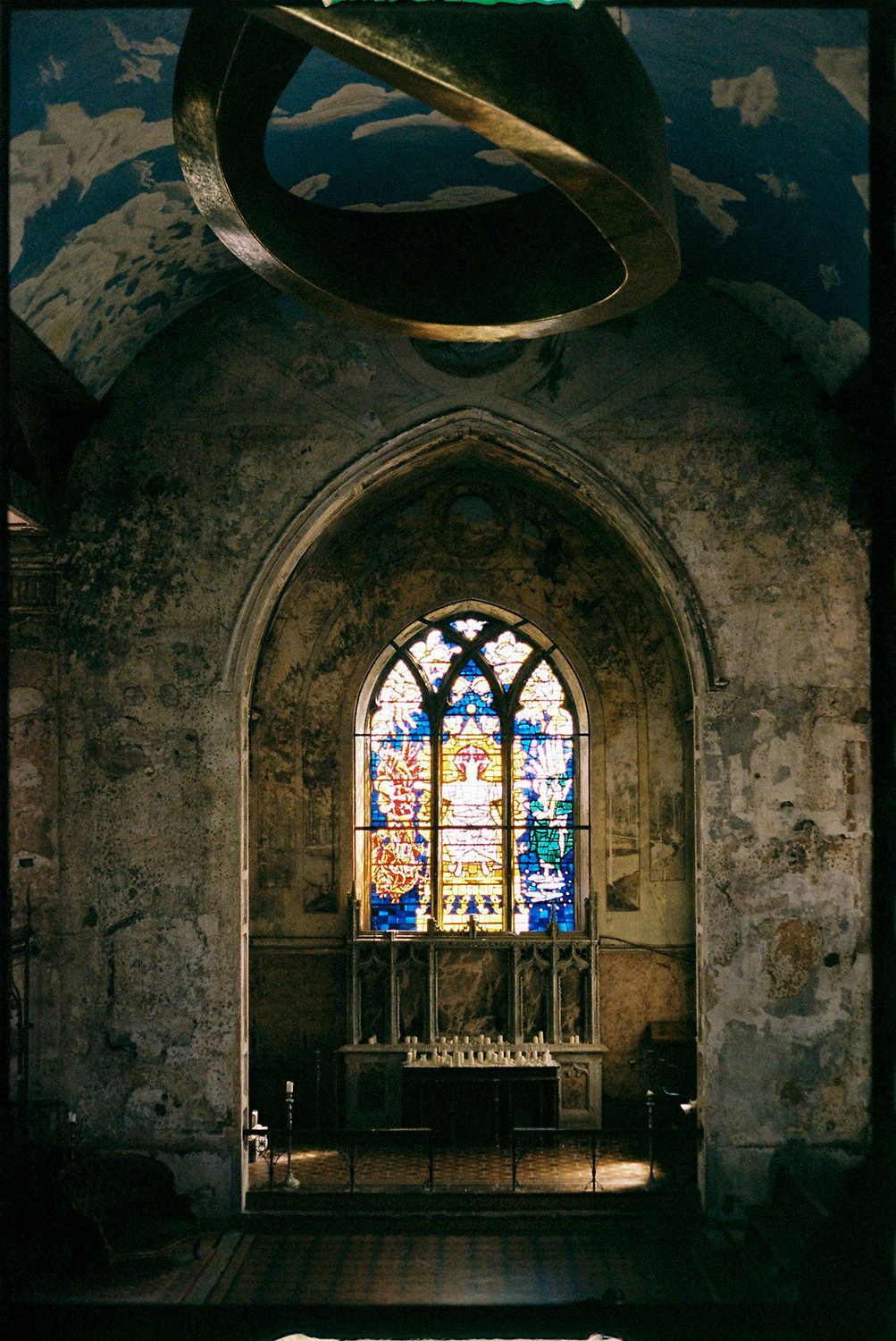 Stained glass windows illuminate the dark stone interior of a historic church or cathedral with colorful light.