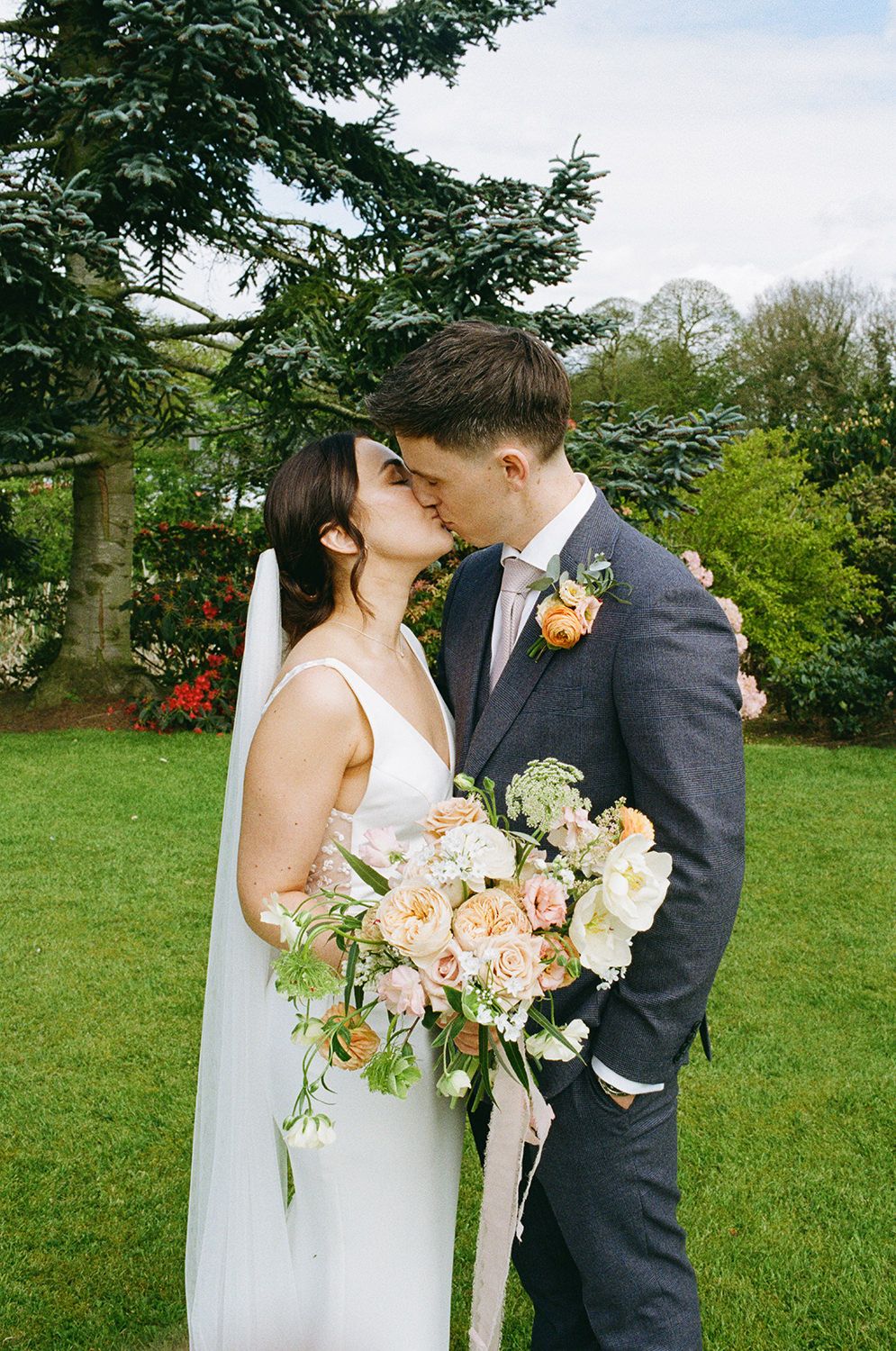 35mm film image of bride and groom kissing in the gardens at The Holford Estate surrounding them.