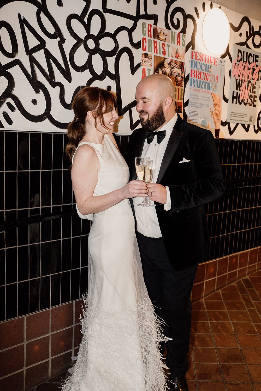 A couple dancing together at a wedding reception against a graffiti wall background.