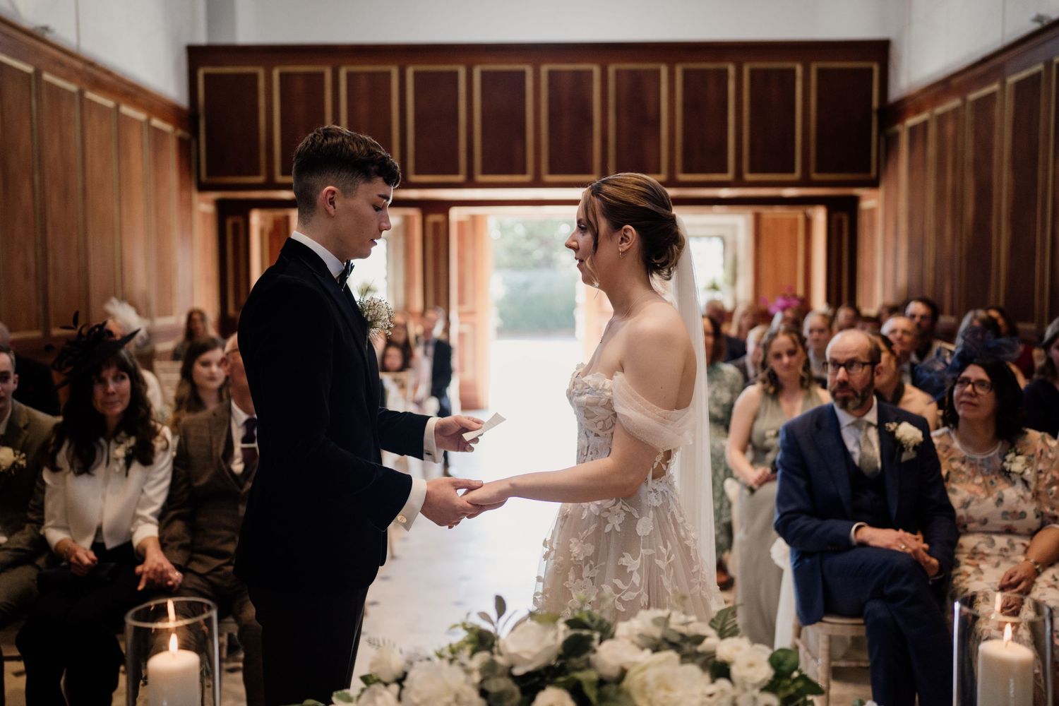 Couple exchanging vows at Bourton Hall with guests in the background.