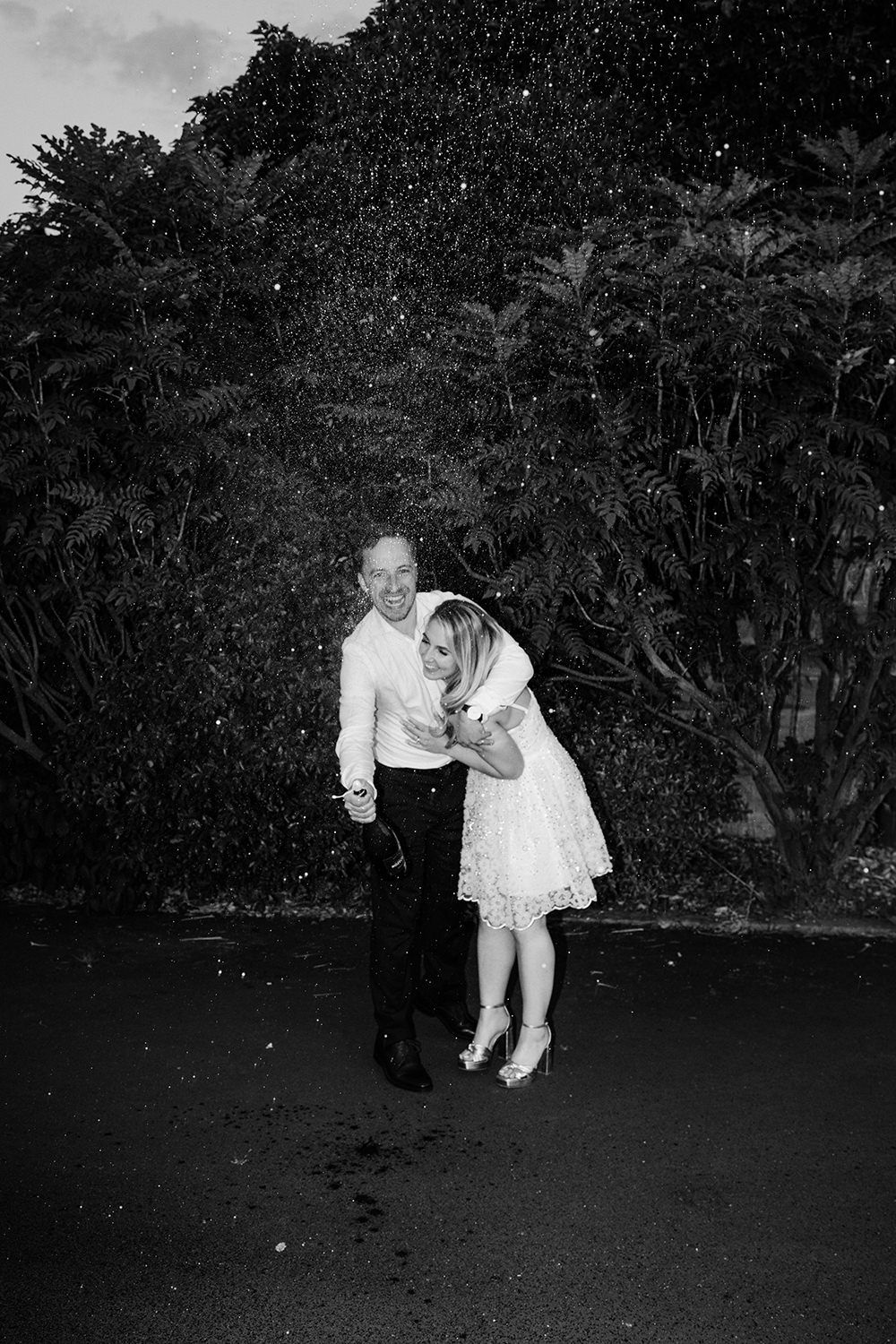 Bride and groom laughing as they spray a bottle of champagne towards the camera.