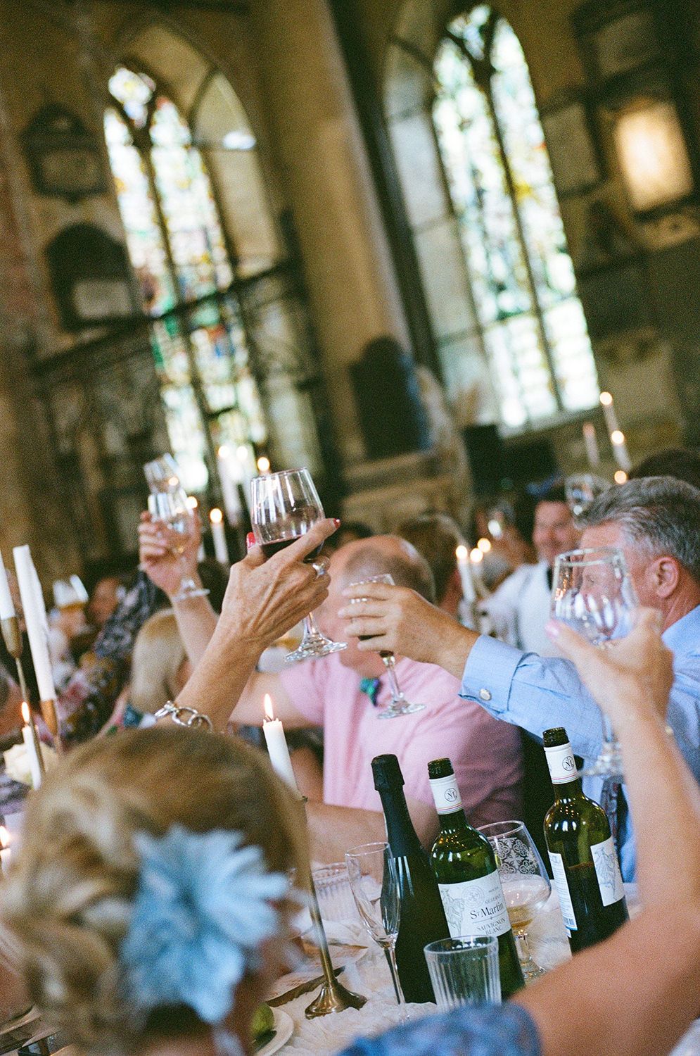 Wedding guests raise their wine glasses in a toast during an indoor reception celebration.