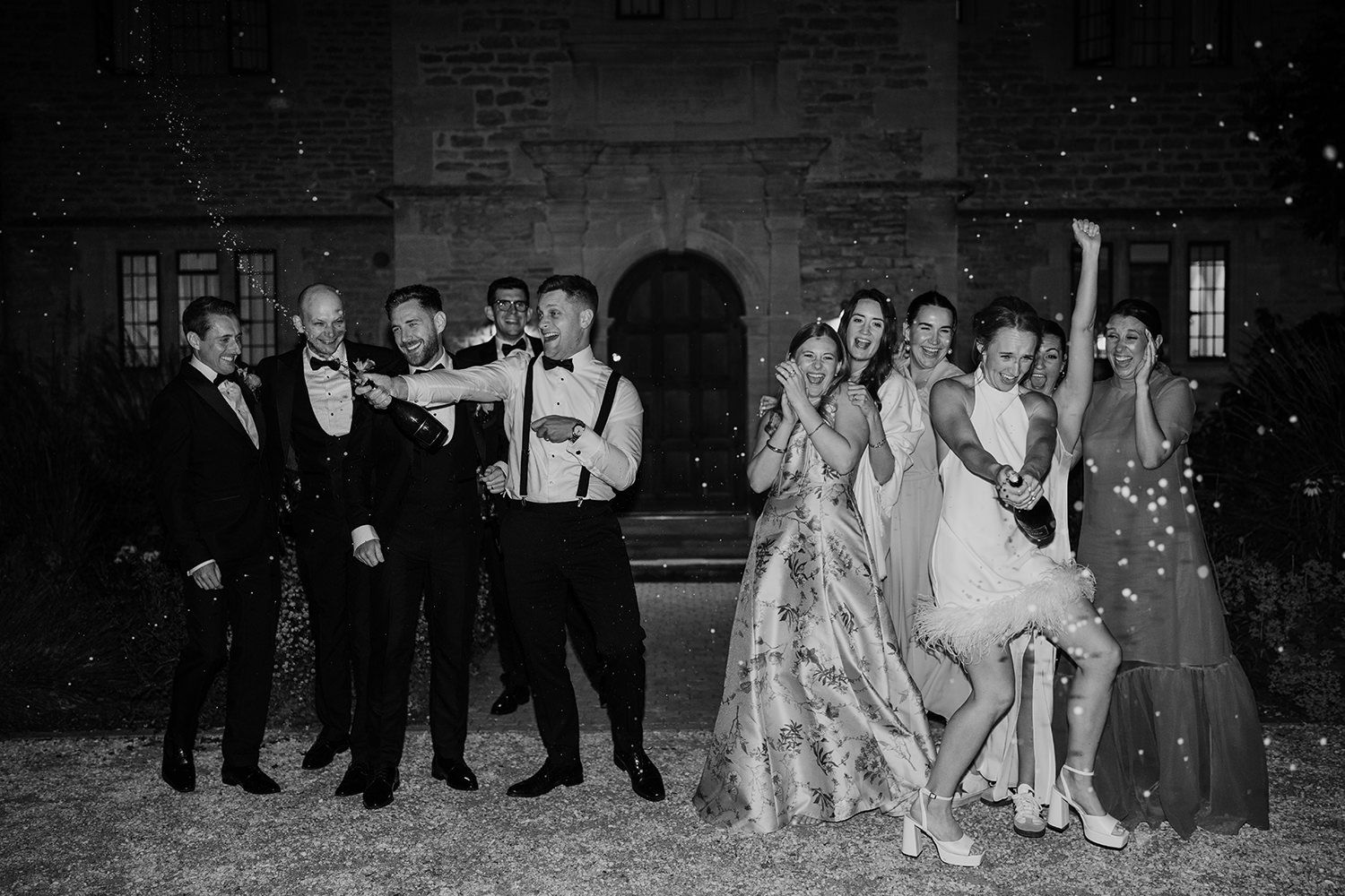 A black and white photo of a wedding party posing outdoors at night with snowflakes falling around them.