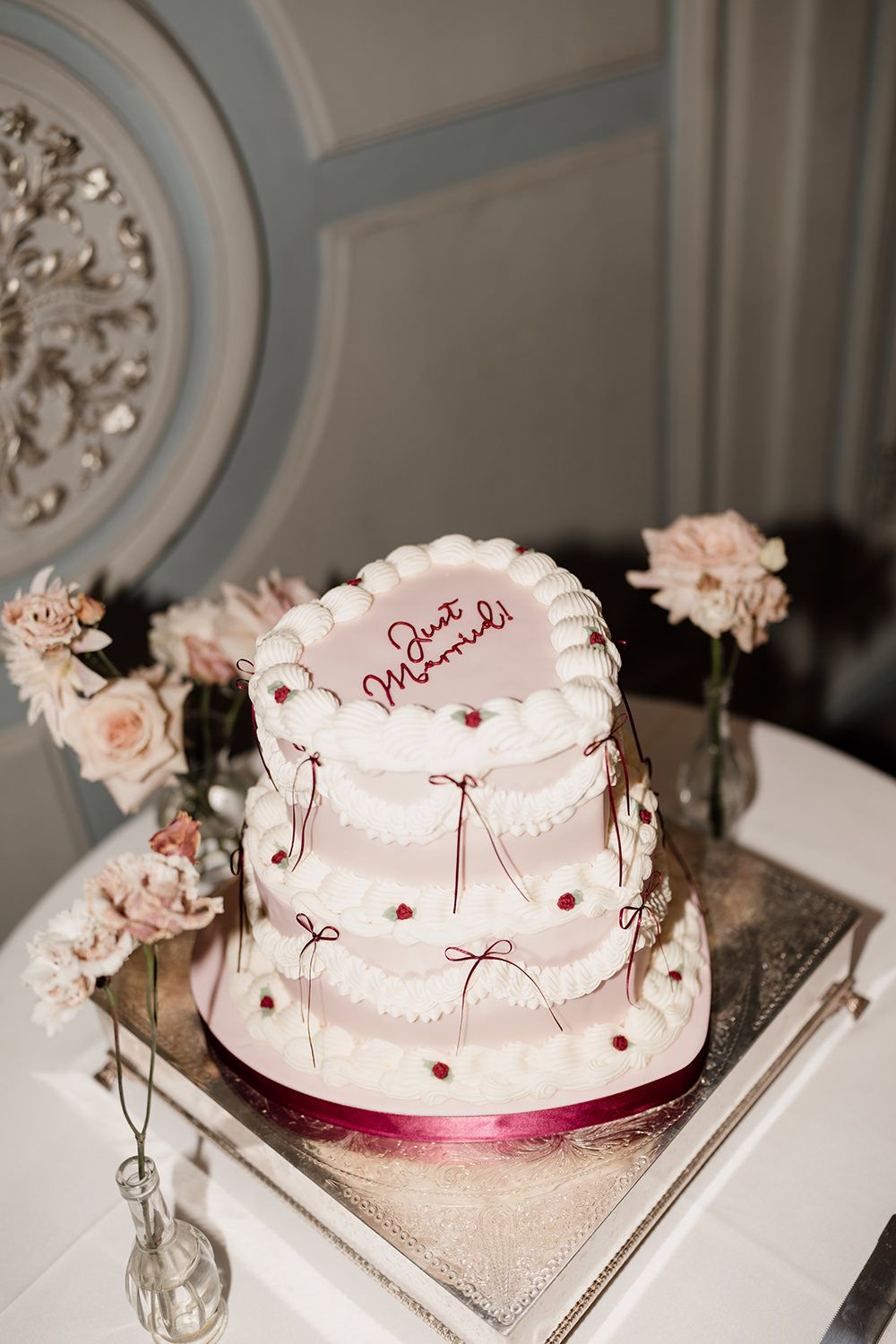 A three-tiered white wedding cake decorated with pink bows and ornate details sits on a silver tray.