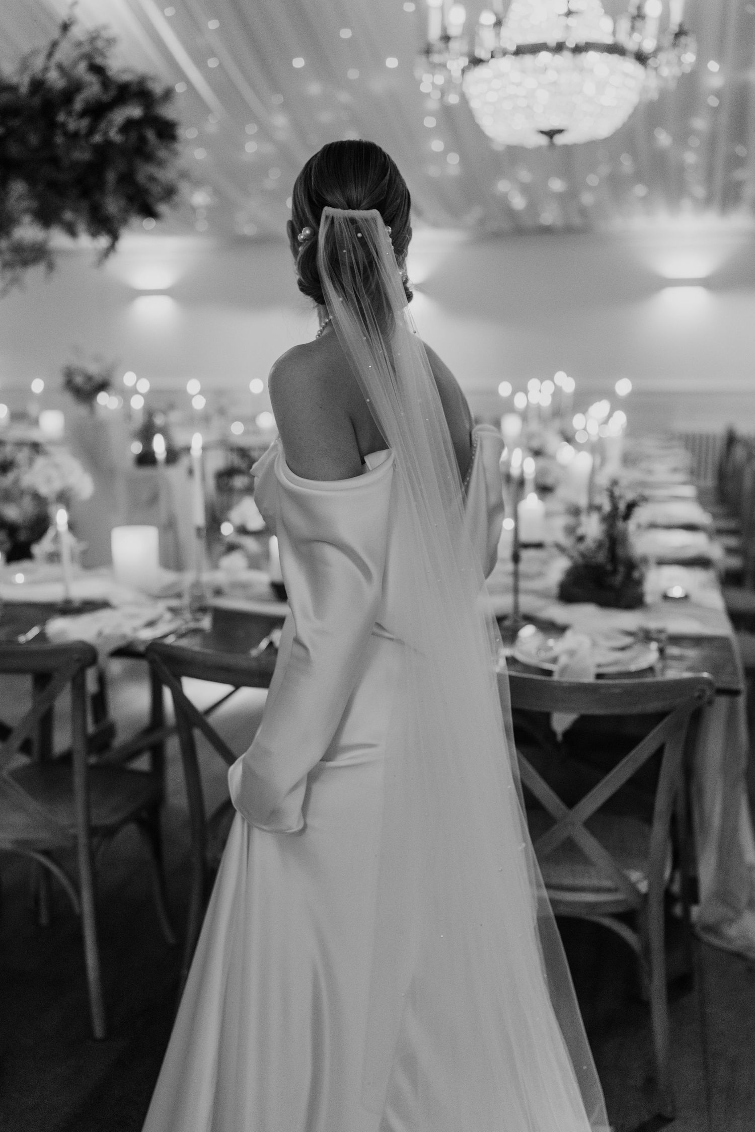 Back view of a white wedding gown with flowing veil in an elegantly decorated reception hall.