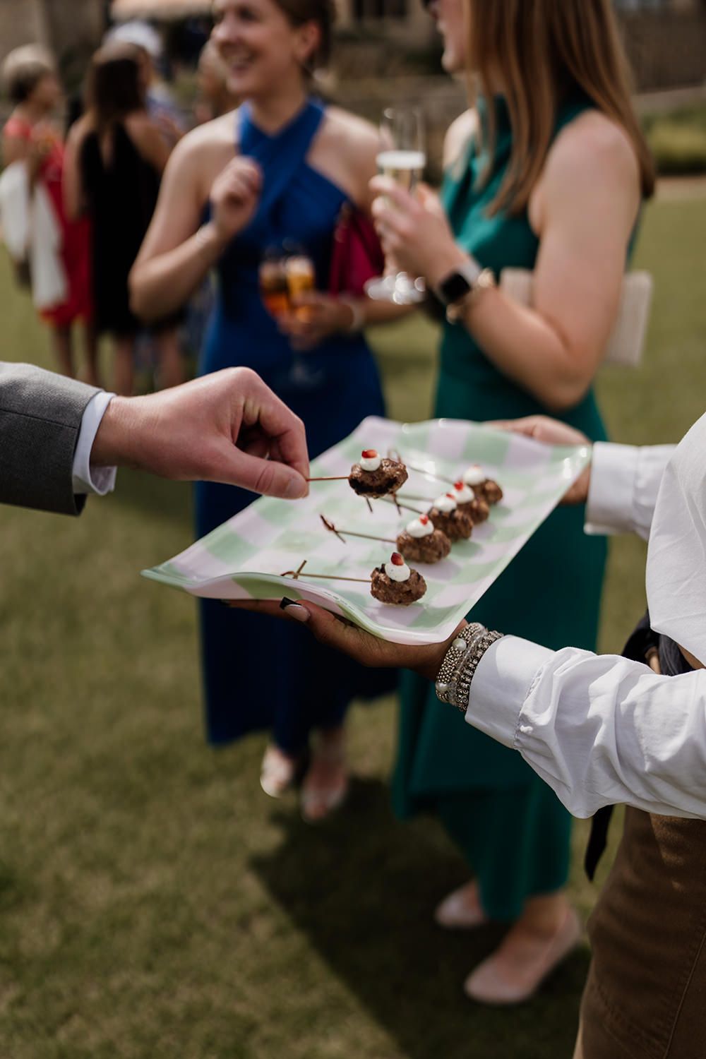 Guests enjoying wedding canapés on a green and white checkered tray.
