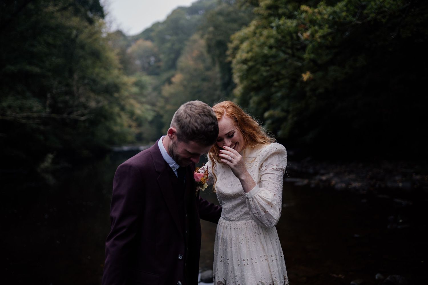 Couple laughing on their wedding day with trees in the background.