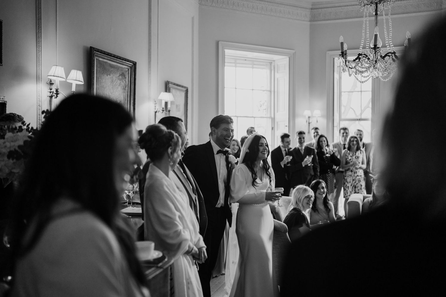Bride and groom laughing with friends and family around them during speeches.