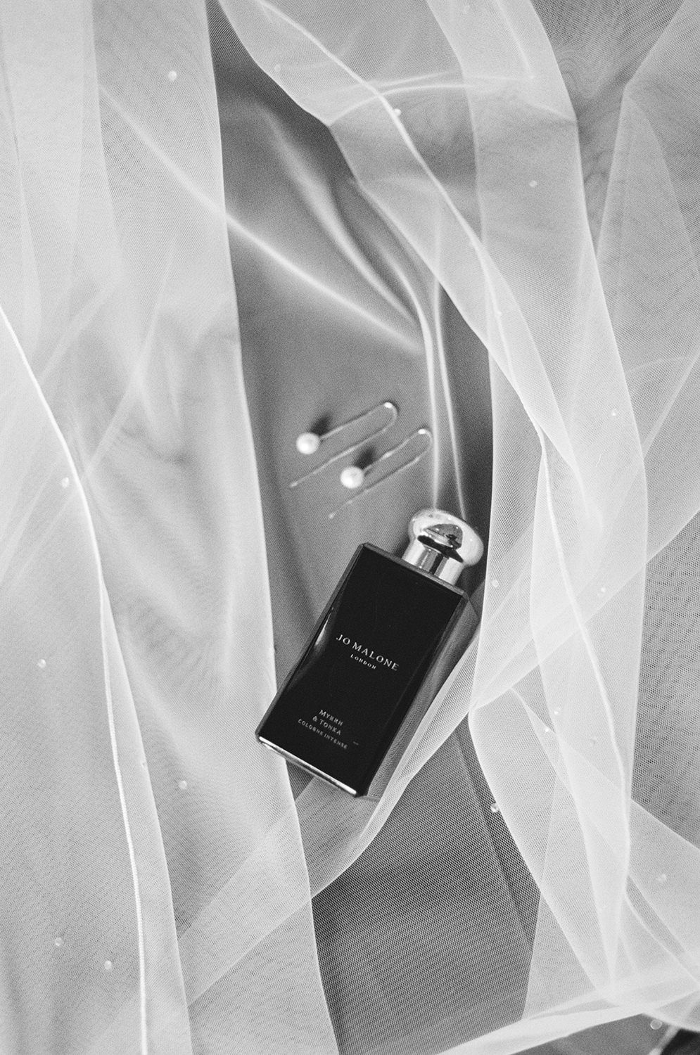 Black Jo Malone perfume and silver pearl earrings on a white wedding veil.