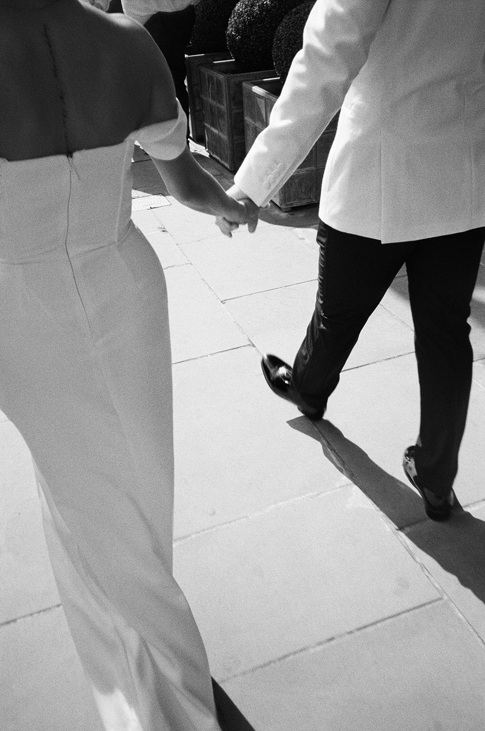 Two people walking together on a white tiled surface, shot in black and white with focus on their legs and shoes.