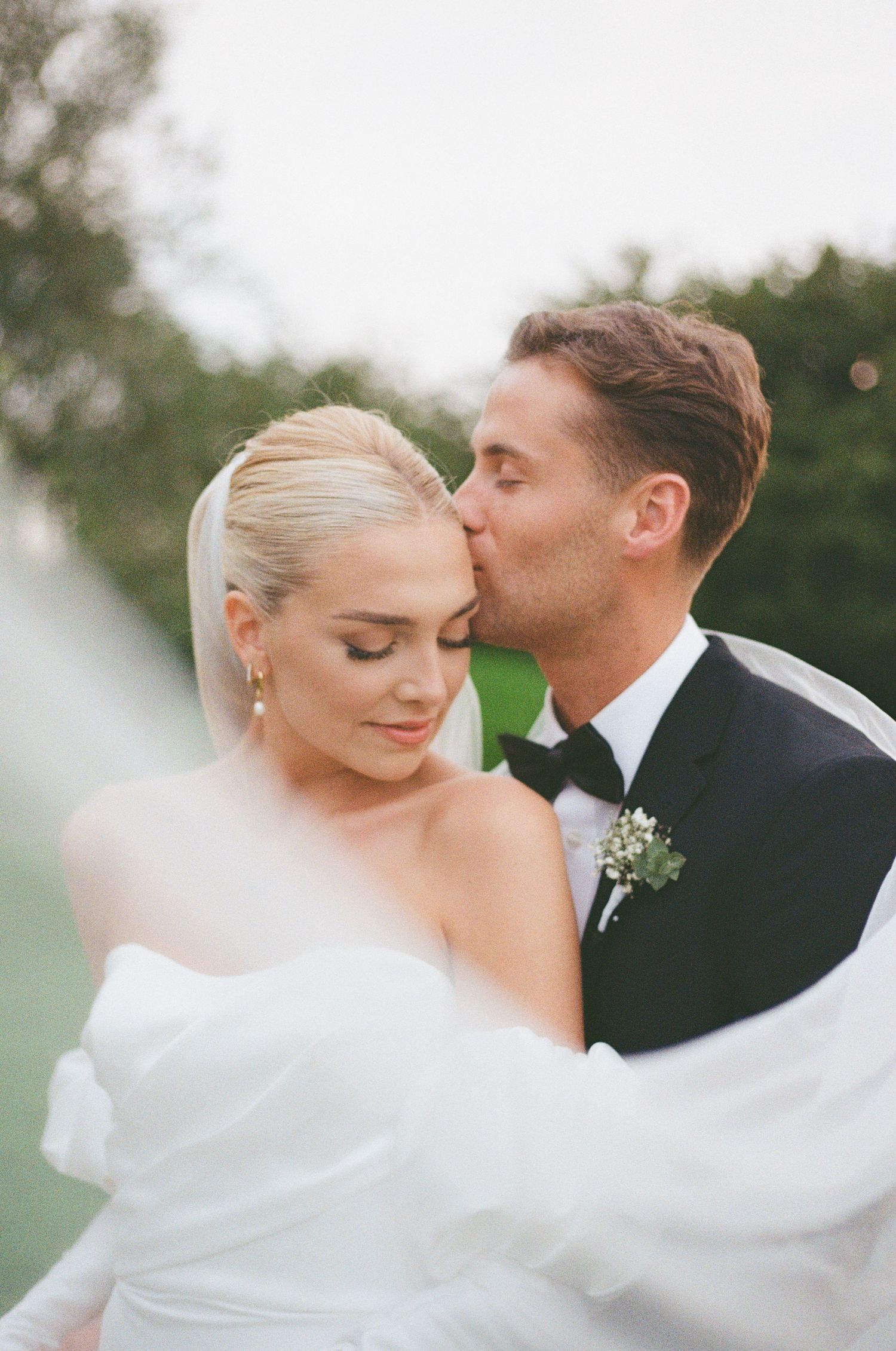 A romantic wedding portrait of a couple sharing an intimate moment outdoors in natural lighting.