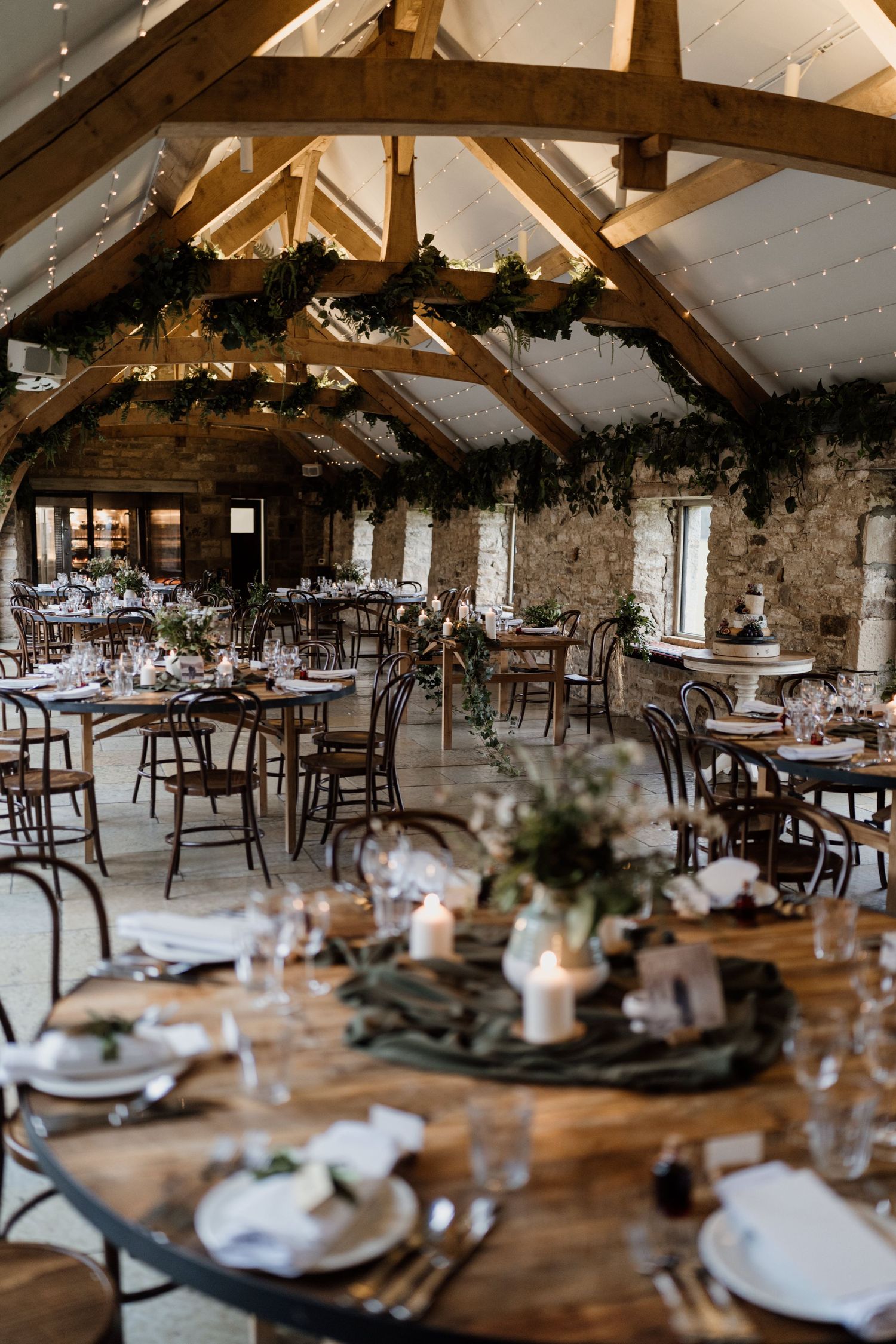 Rustic wedding reception venue with exposed wooden beams, stone walls and elegant table settings in a barn-style interior.