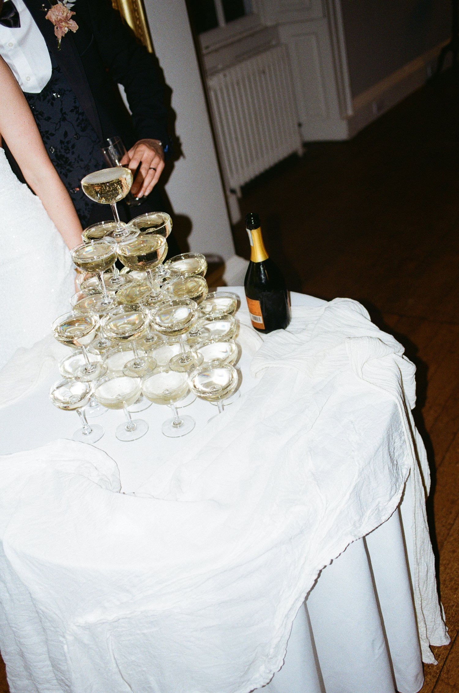 Champagne glasses arranged in pyramid formation on white tablecloth with bottle in background at elegant event.