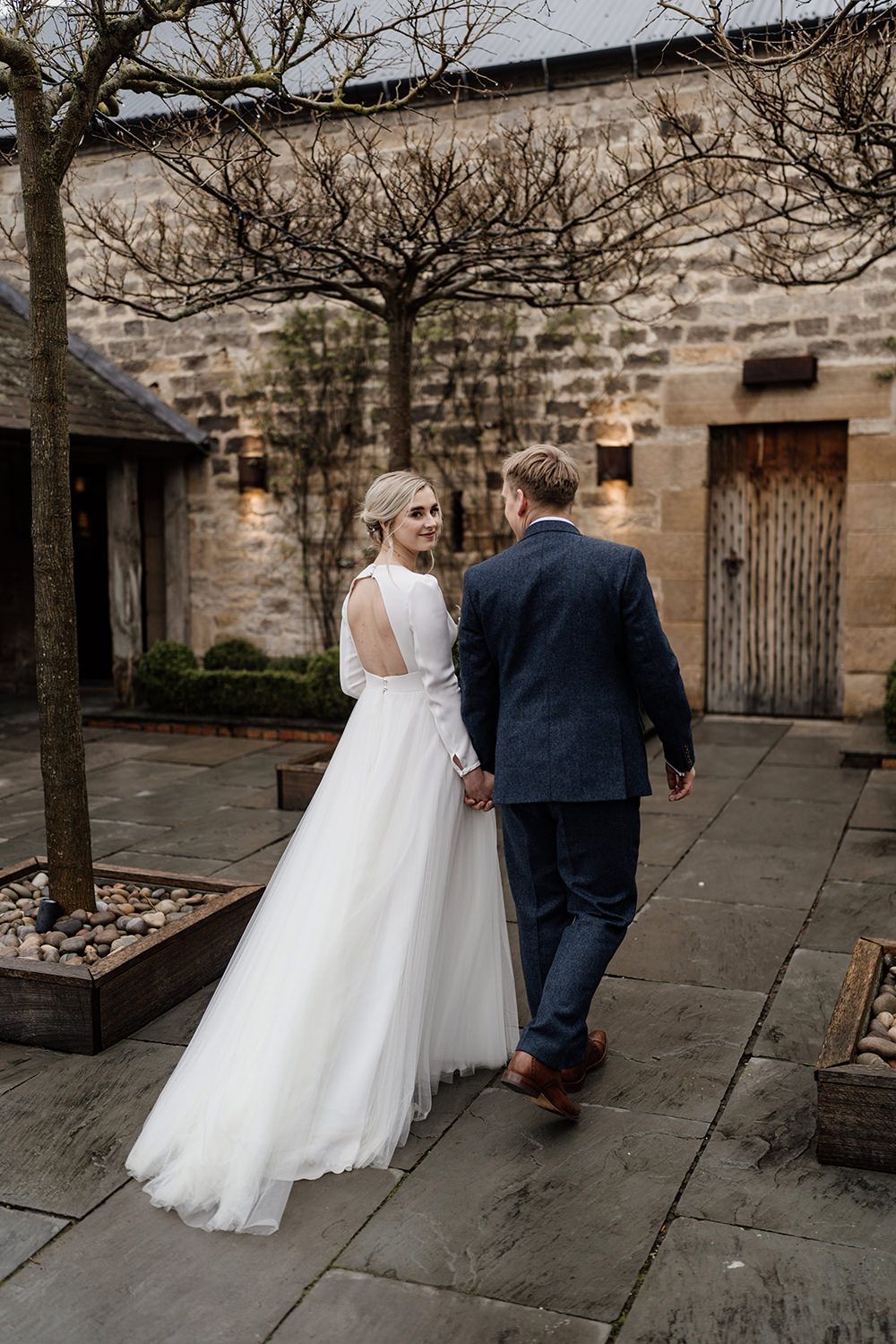 Bride and groom walking away from the camera with Healey Barn in the background.