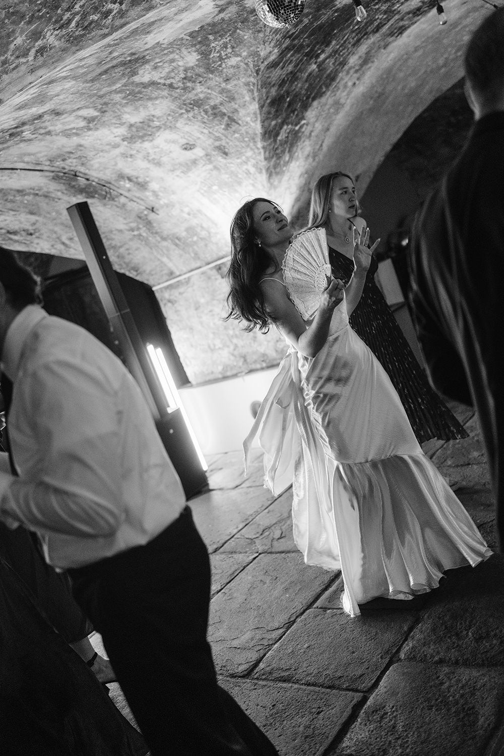 A series of black and white photographs showing figures in white robes dancing and moving in a dark stone space.