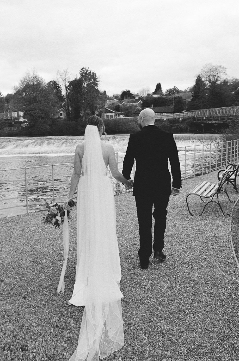 Bride and groom holding hands walking by the River Derwent.