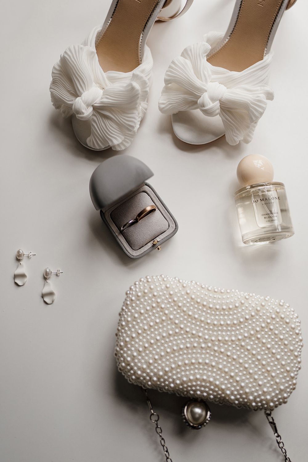 White table with bridal shoes, rings, perfume, earrings and bag scattered on top.